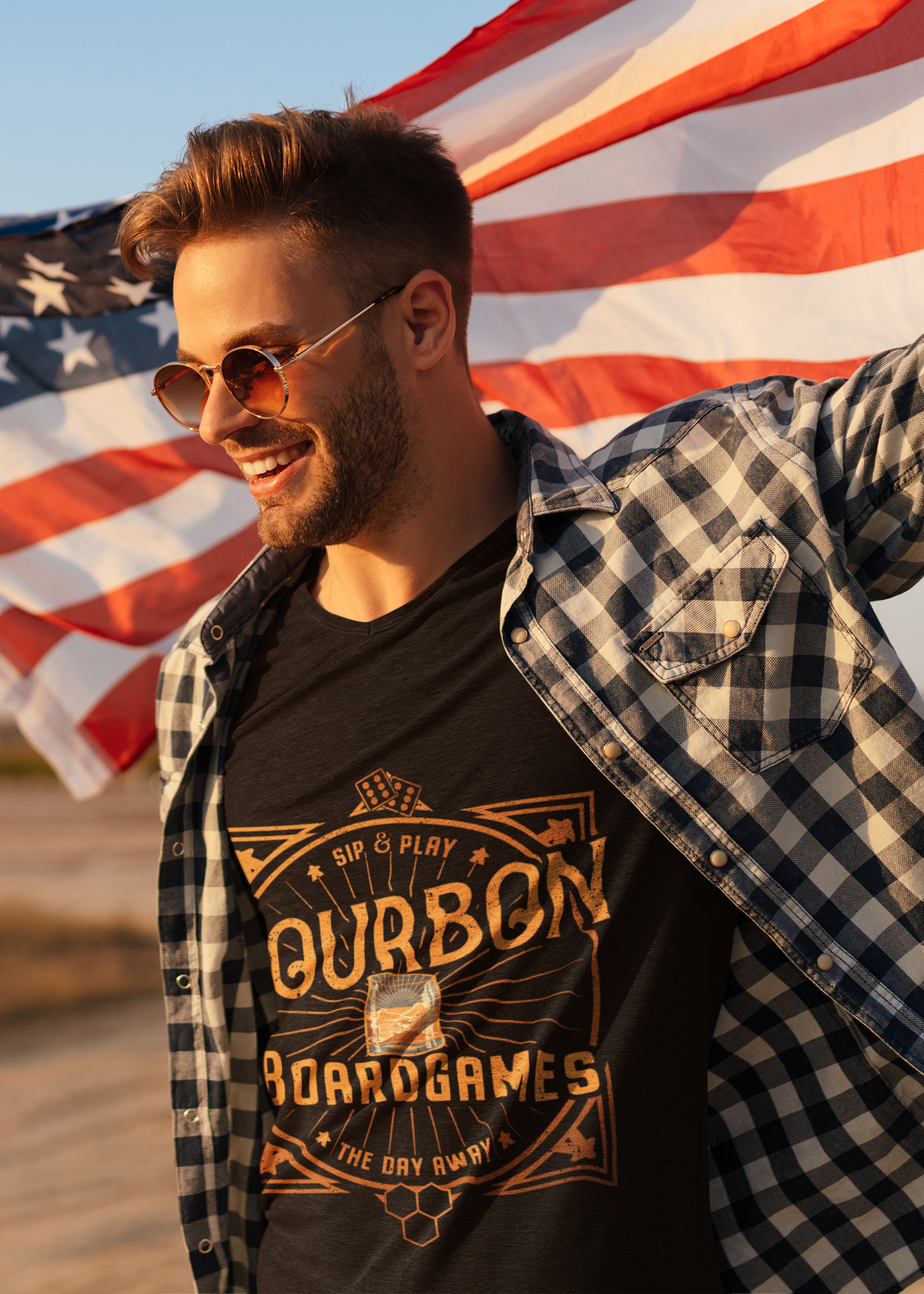 Man wearing sunglasses and a black t-shirt with ' bourbon boardgames' design, standing in front of an American flag.