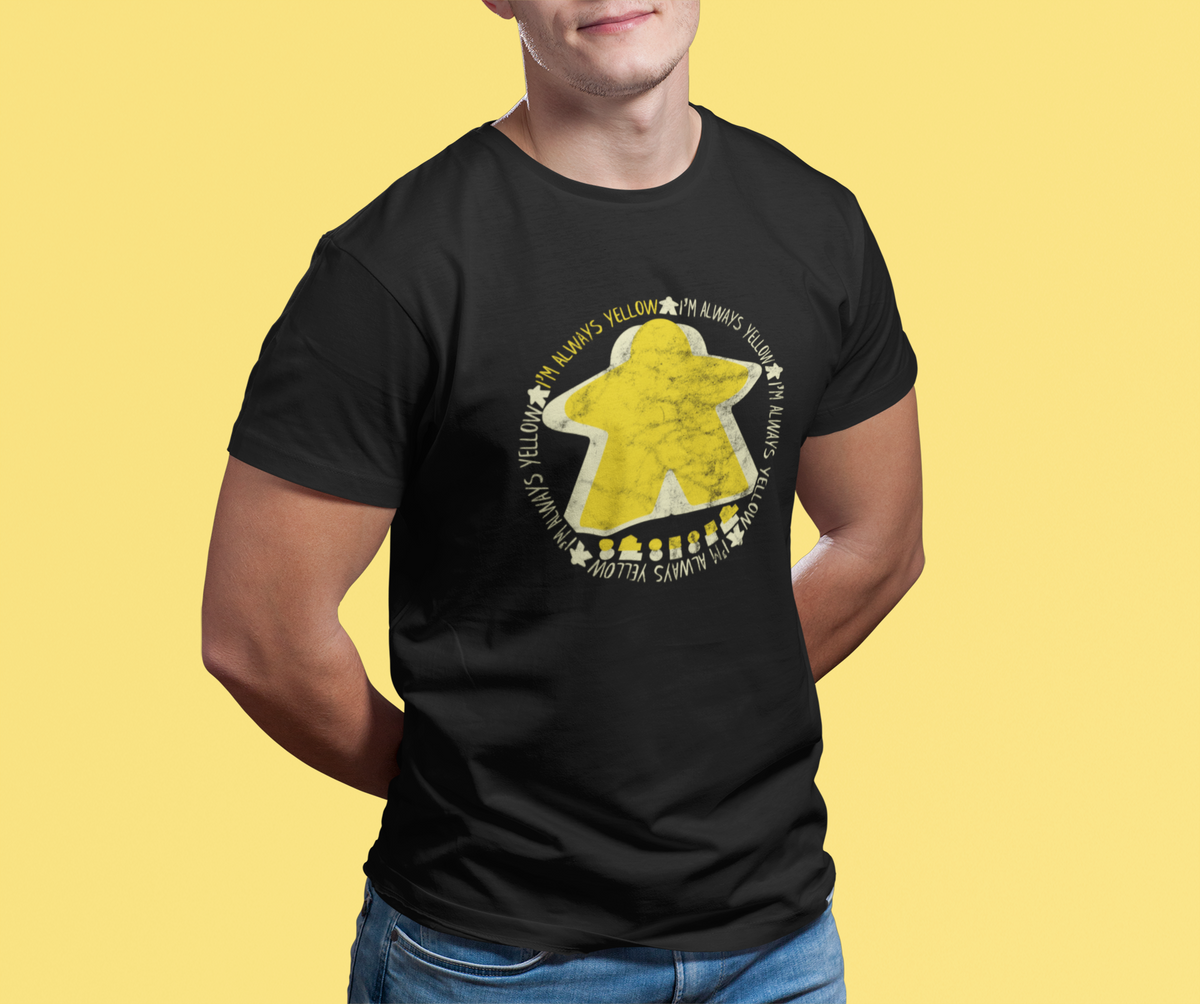 Person wearing a black t-shirt with our I'm Always Yellow Meeple design on a yellow background