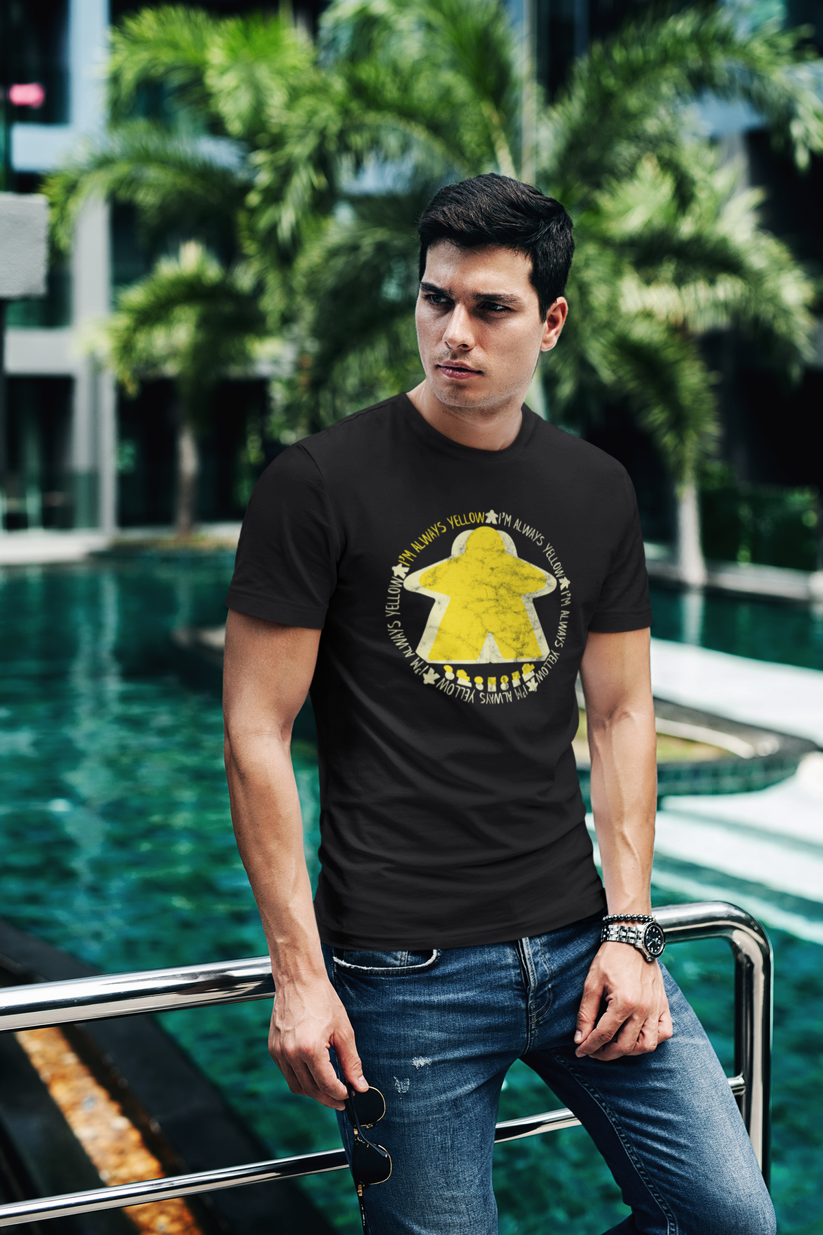 Man wearing a black t-shirt with our I'm Always Yellow Meeple design by a poolside