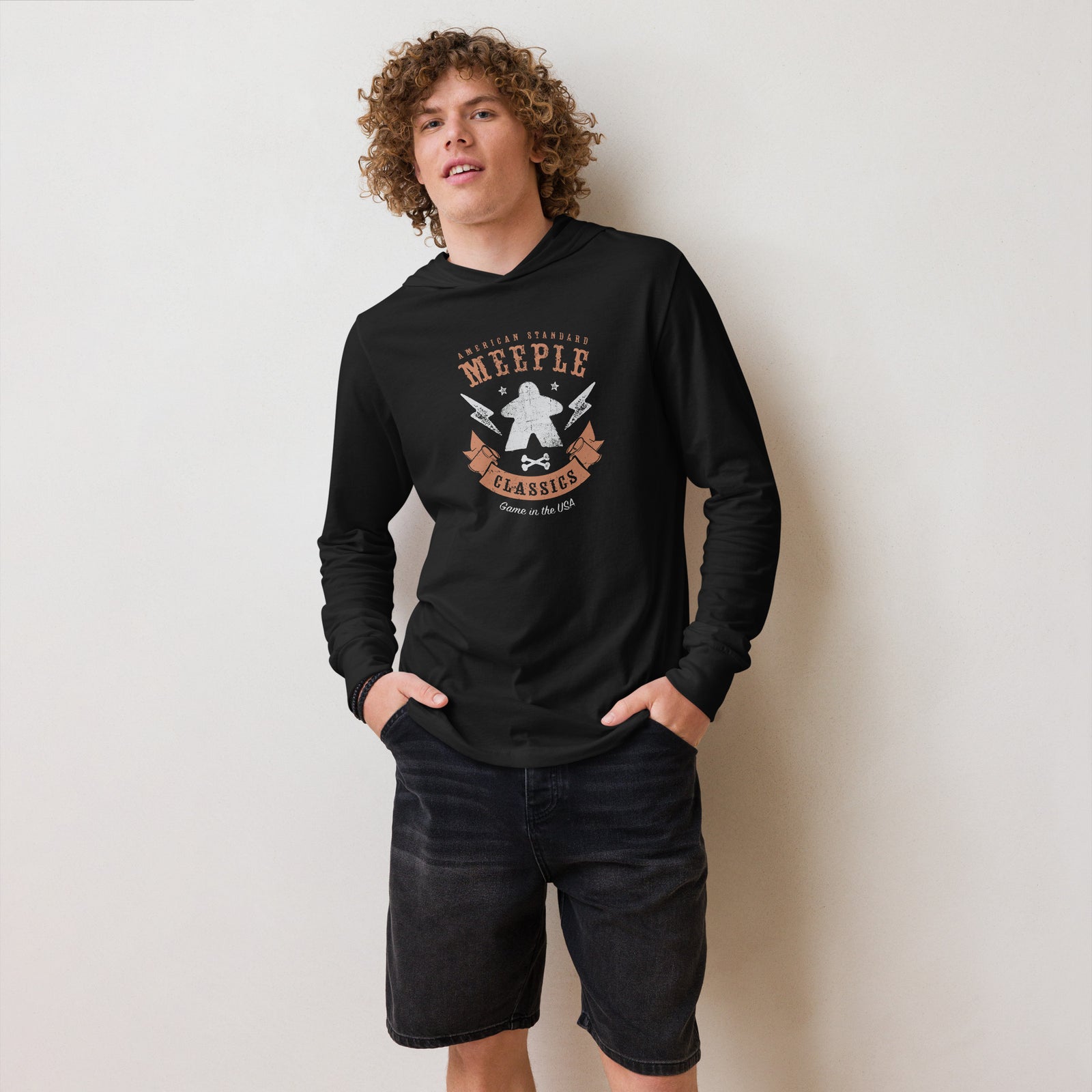 Model leaning against wall and wearing long sleeve American Meeple Classics t-shirt