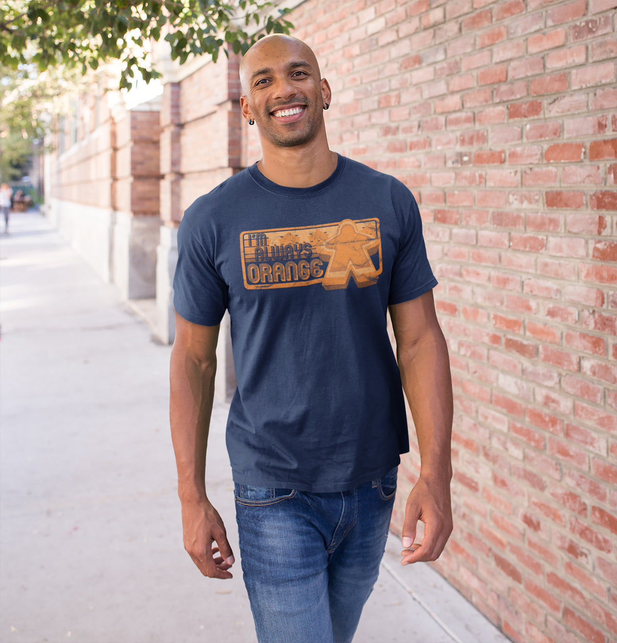 Man wearing a navy blue t-shirt with our I'm Always Orange design, standing against a brick wall.