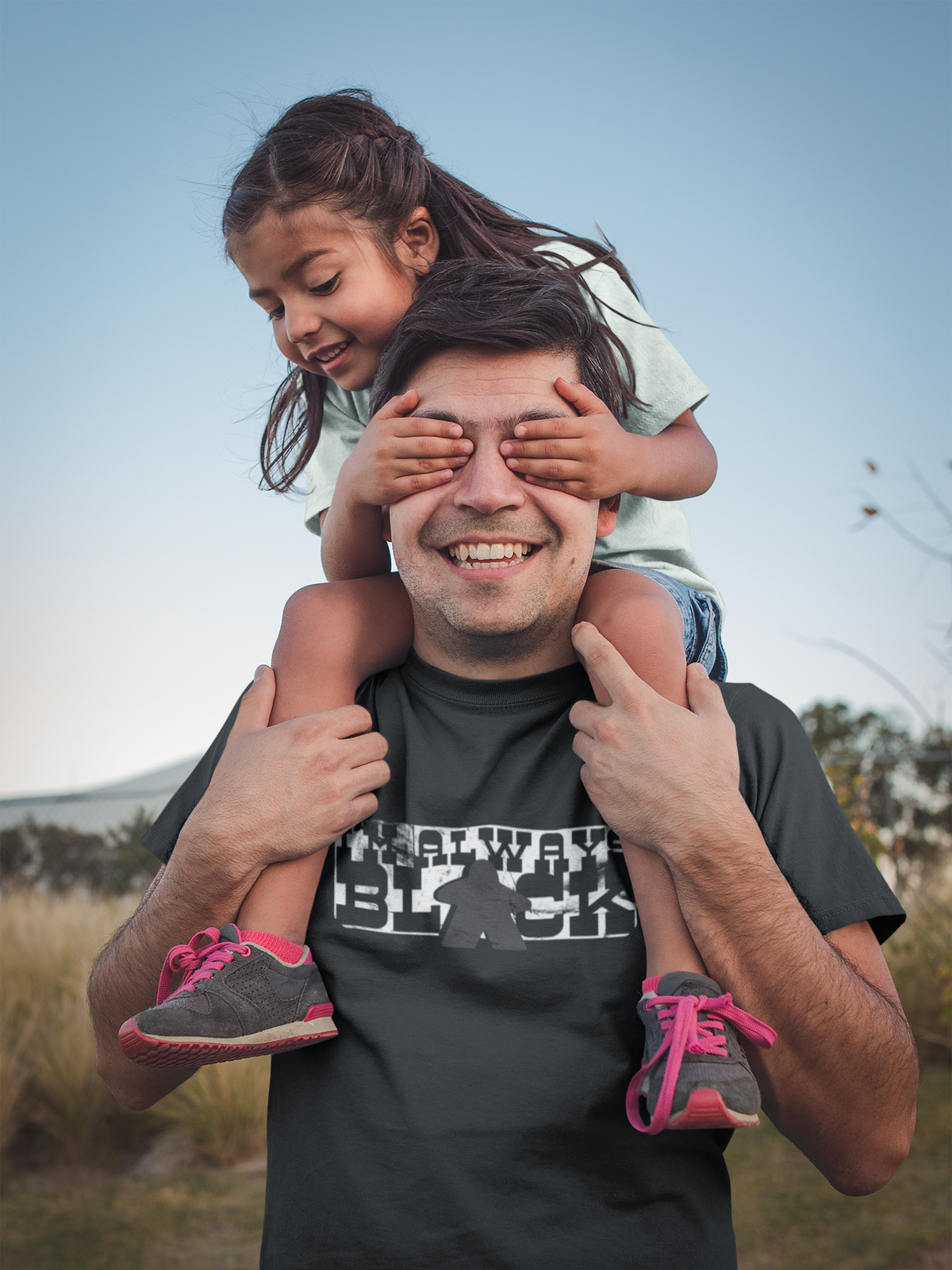 Man with a child on his shoulders outdoors wearing our I'm Always Black t-shirt