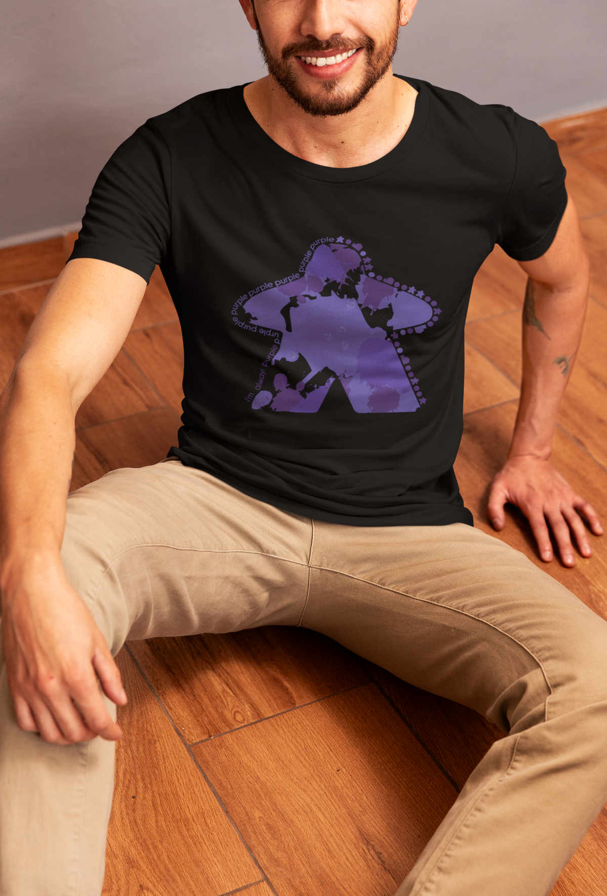 Man wearing a black t-shirt with our I'm Always Purple design sitting on a wooden floor.