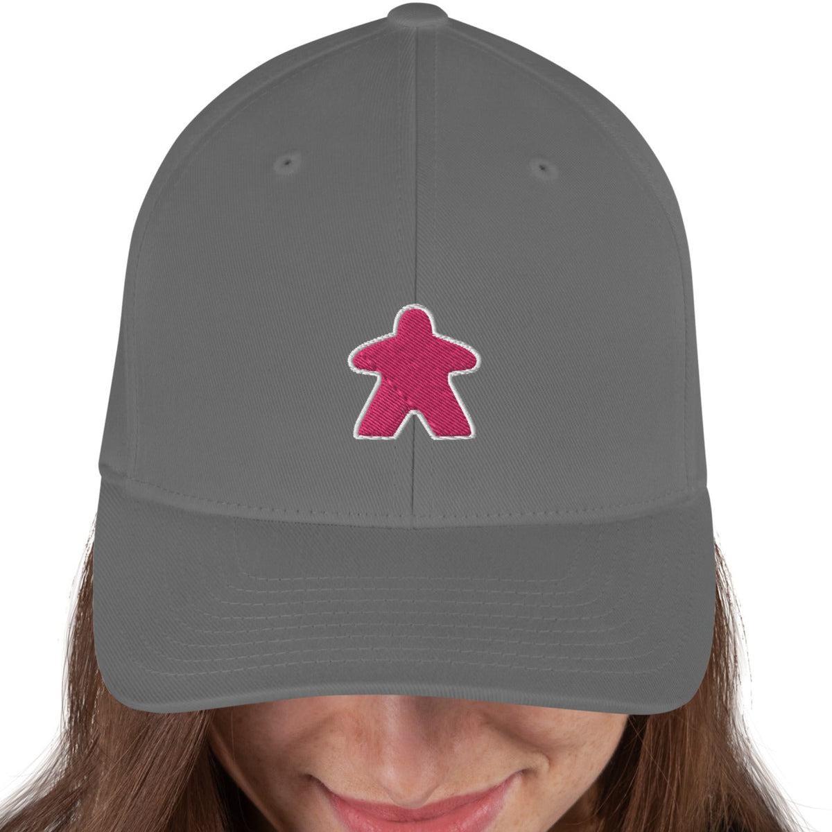 Model wearing a grey flexfit board game hat with our pink meeple embroidered on the front